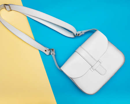 White woman leather hand bag with long handle on blue and yellow background. Flat layの写真素材