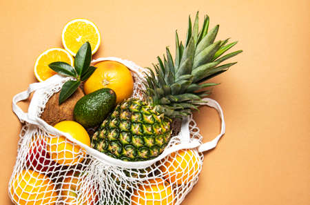 Mesh shopping bag with organic fruits on light brown background. Flat lay, top view. Zero waste, plastic free concept. Healthy clean eating diet and detox. Summer fruits.の写真素材