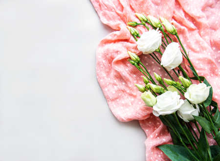 White beautiful eustoma flowers on white background with pink dotted scarf. Flat lay.の写真素材
