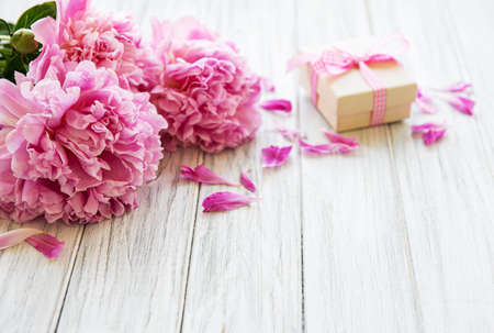 Background with pink peonies and gift box on white wooden boardの写真素材