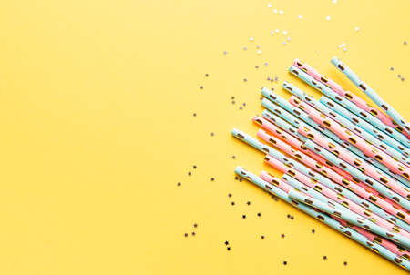 Drinking straws for party and silver stars confetti on yellow background with copy space. Top view of colorful paper disposable eco-friendly straws for summer cocktails.の写真素材