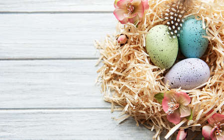 Colorful Easter eggs in nest on wooden background. Minimal easter concept. Easter card with copy...