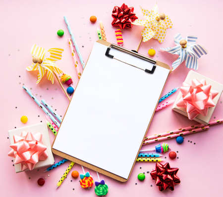 Clipboard and colorful decorations on pink pastel background. Flat lay, top view. Birthday background, holiday concept. の写真素材