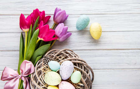 Easter background with colorful eggs in nest and pink tulips on a white wooden background. Top view with copy spaceの写真素材