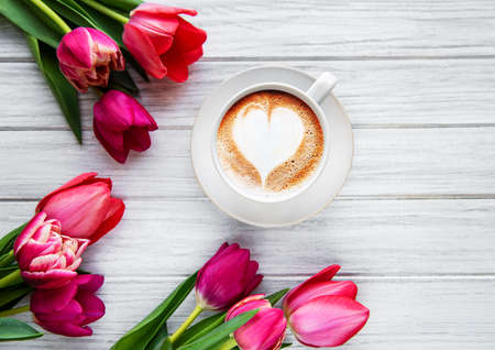 Coffee cup with latte art and pink tulips on the wood table. Top view, flat lay. の写真素材