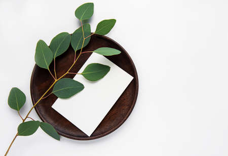 Wooden  plate with eucalyptus on white background, top view, mockupの写真素材