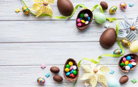 Easter composition with colorful and chocolate eggs on white wooden background, space for text. Top...