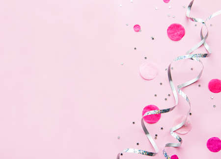 Festive minimal flat lay style composition with silver ribbons and pink confetti over pinkの写真素材
