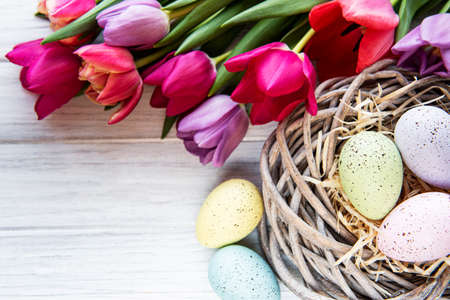 Easter background with colorful eggs in nest and pink tulips on a white wooden background. Top view...