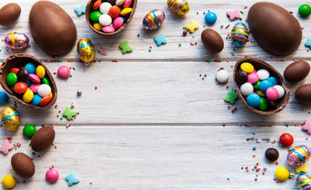 Easter composition with colorful and chocolate eggs on white wooden background, space for text. Top...