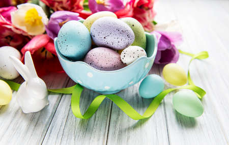 Easter background with colorful eggs in bowl and pink tulips on a white wooden background. Top view...