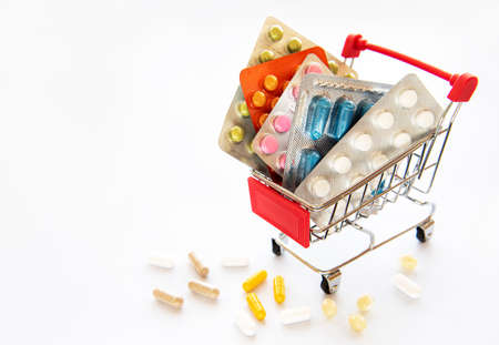 Miniature shopping cart filled with pills, tablets and capsules: pharmacy shopping, medicine and...