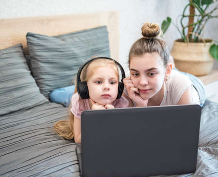 Two sisters  study on the computer online at home in bed. Distance learning quarantined. Stay home concept.の写真素材
