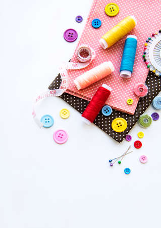 Sewing accessories and fabric on a white background. Sewing threads, needles, pins, fabric, buttons and sewing centimeter. Top view, flat lay.の写真素材