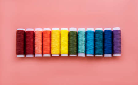 Spools of thread on the colors of the rainbow on a pink background, flat lay