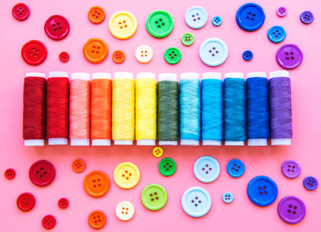 Spools of thread and buttons on the colors of the rainbow on a pink background, flat layの写真素材
