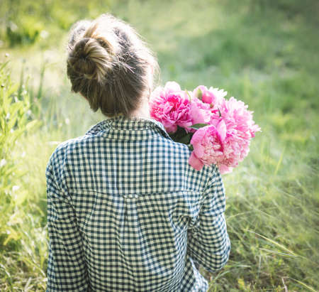 Portrait of a beautiful girl with a bouquet of peonies, view from the backの写真素材