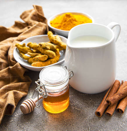Ingredients for turmeric latte. Ground turmeric, curcuma root, cinnamon, jug of milk over gray concrete background. Top view, copy spaceの写真素材