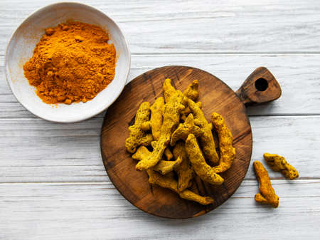Bowls with turmeric powder and dry roots on a wooden backgroundの写真素材