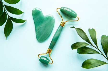 Jade face roller for beauty facial massage therapy. Flat lay on pastel green background