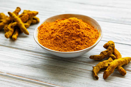 Yellow turmeric powder and dry roots on wooden background.