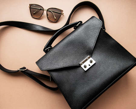 Black leather bag with sunglasses on a brown backgroundの写真素材