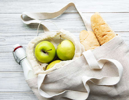 Fresh apples, milk and bread in eco cotton bag on a white wooden tableの写真素材