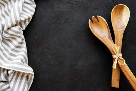 Two wooden salad spoons on a black stone background, flat layの写真素材