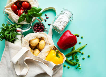 Fresh vegetables in eco cotton bags on green background. Zero waste shopping concept.の写真素材