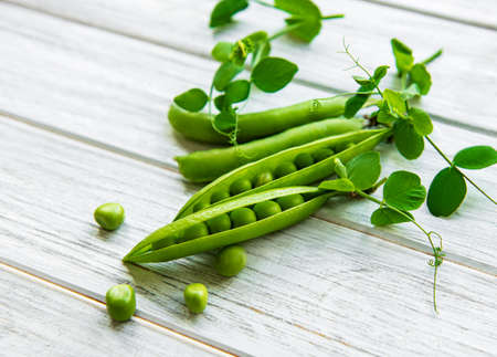 Pods of green peas with pea leaves on a white wooden background. Organic food.の写真素材