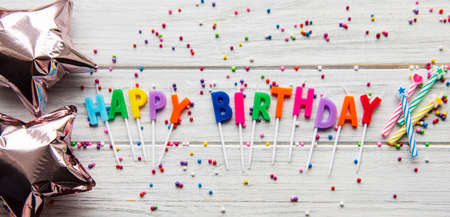Text Happy Birthday by candle letters with birthday asseccories, candles and confetti on white wooden backgroundの写真素材