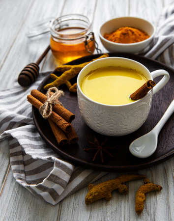 Yellow turmeric latte drink. Golden milk with cinnamon, turmeric, ginger and honey over white wooden background.の写真素材