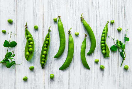 Pods of green peas with pea leaves on a white wooden background. Organic food.