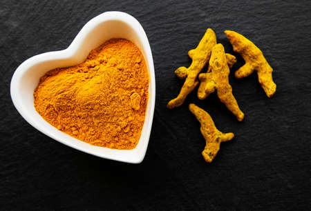 Bowl with turmeric powder and dry roots on a black concrete backgroundの写真素材
