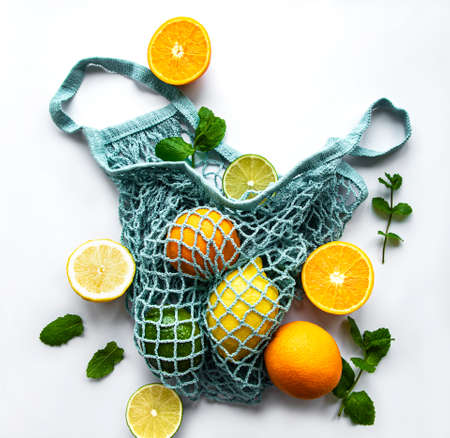Ripe whole citrus fruits in string bag on white background