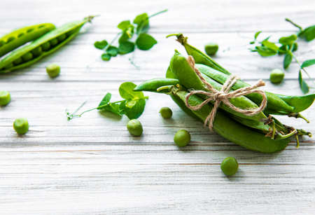 Pods of green peas with pea leaves on a white wooden background. Organic food.の写真素材