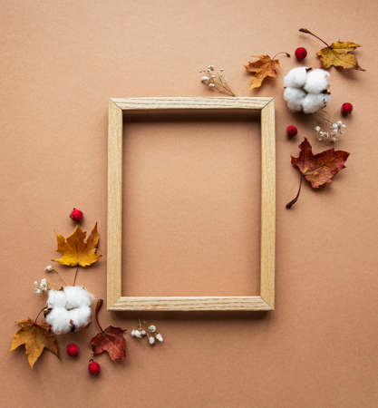 Autumn composition. Photo frame, flowers, leaves on brown background. Autumn, fall, thanksgiving day concept. Flat lay, top view, copy spaceの写真素材