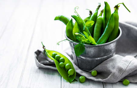 Fresh green peas in a small metal bucket on old wooden backgroundの写真素材