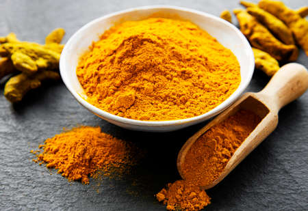 Bowl with turmeric powder and dry roots on a black background