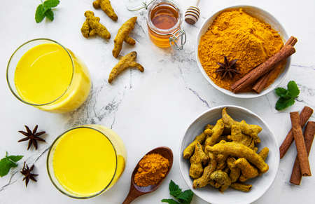 Yellow turmeric latte drink. Golden milk with cinnamon, turmeric, ginger and honey over white wooden...