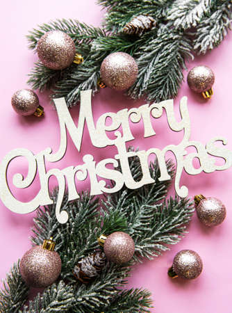Branches of a Christmas tree and decorations on a pink pastel background with the wishes of Merry Christmasの写真素材