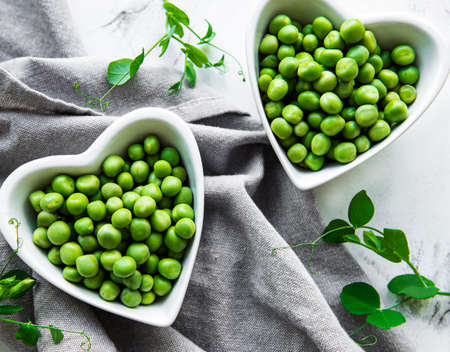 Green peas in heart shaped bowls on a fabric backgroundの写真素材