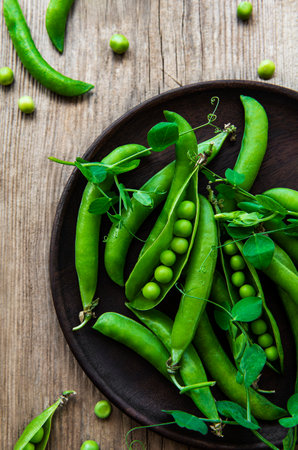 Green peas in a plate on a old wooden background. View from above.の写真素材