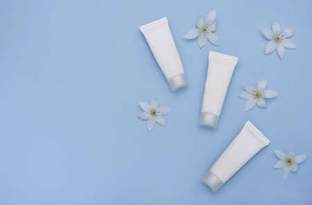 White tubes of cream on a blue background with white flowersの写真素材