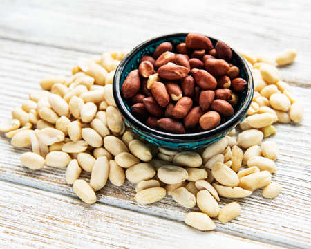 Peeled peanuts in a wooden bowl on a white wooden background
