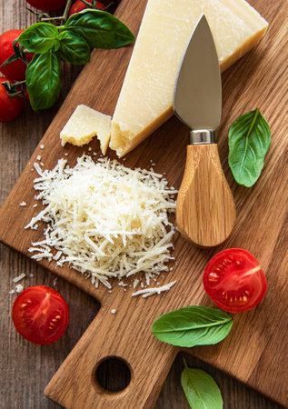 Grated parmesan with basil and tomatoes on a cutting boardの写真素材