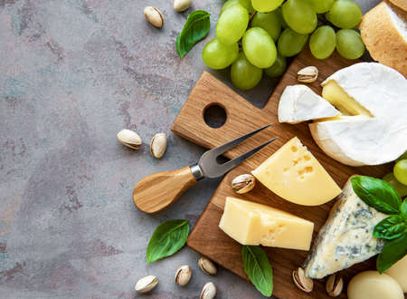 Various types of cheese, grapes and snacks on a gray concrete background