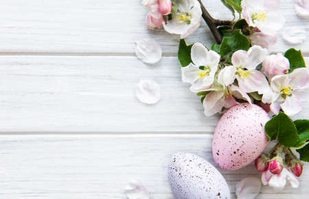 Colorful Easter eggs with spring blossom flowers over wooden background. Colored Egg Holiday border.