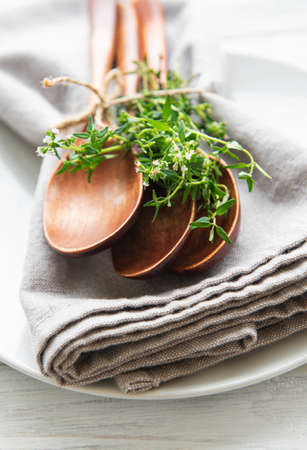 Wooden spoons on a plate and linen napkins decorated with green bunches of thymeの写真素材
