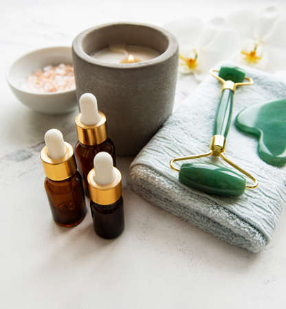 Face massage jade roller with cosmetic product on white marble backgroundの写真素材